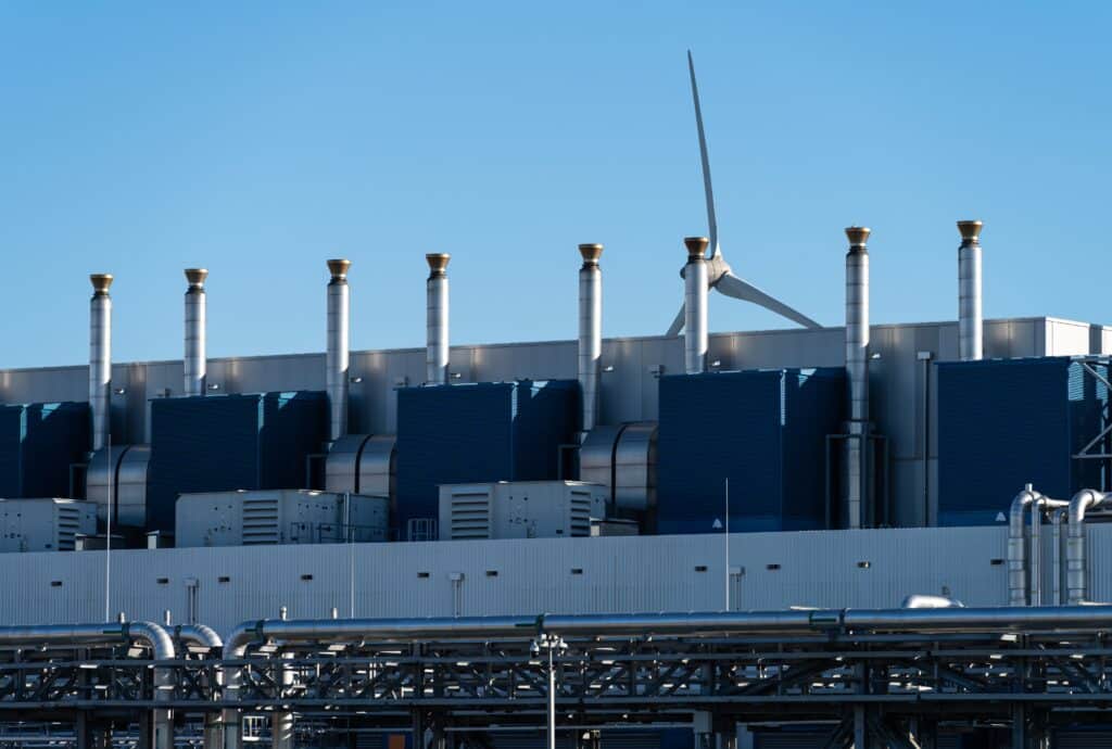 Exterior of a large data center complex with a wind turbine in the background, Shutterstock ID#2084483464