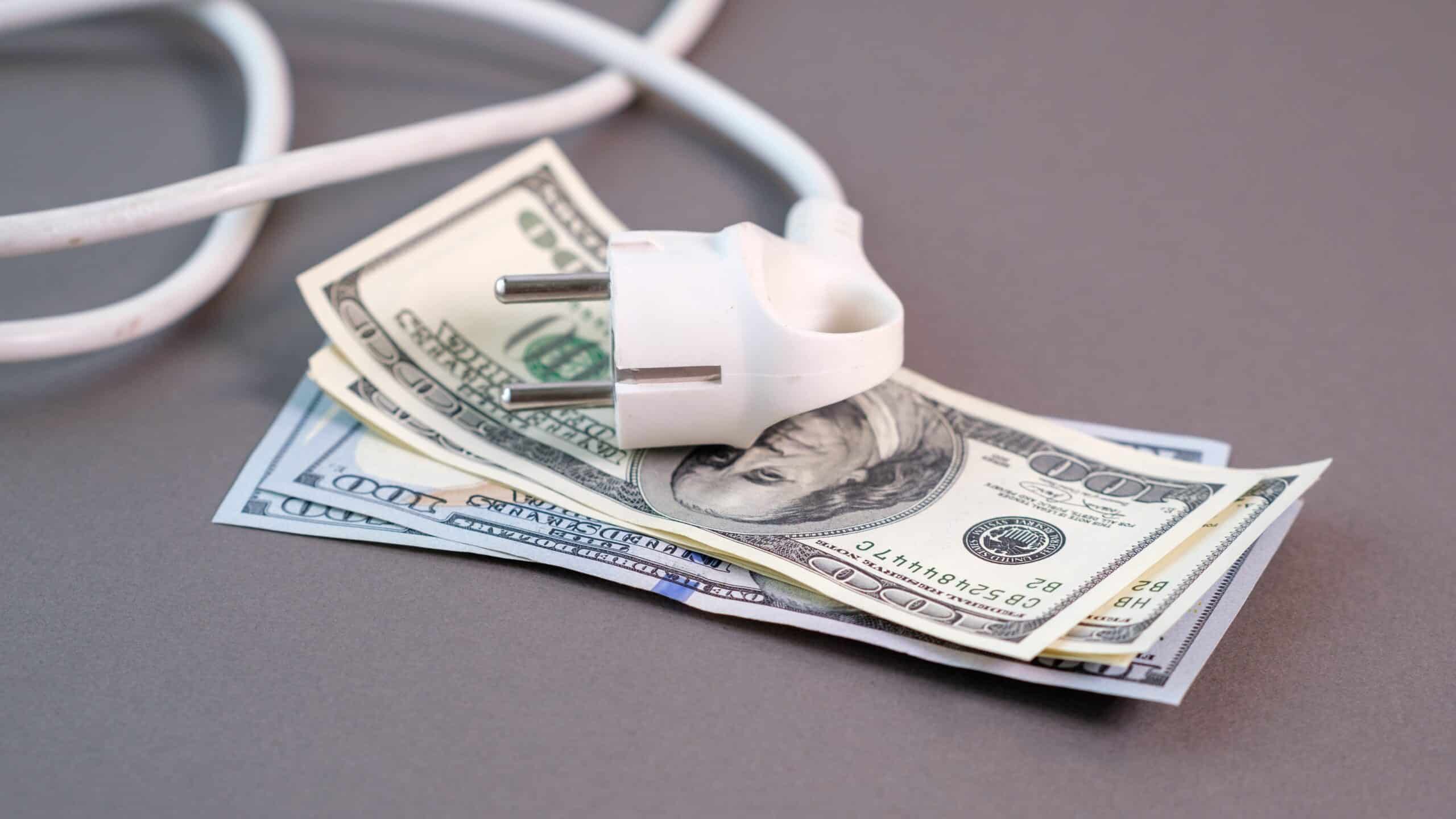 Dollars and a power strip illustrating high electricity prices and the rising cost of household energy during the utility crisis, Shutterstock ID#2719436007