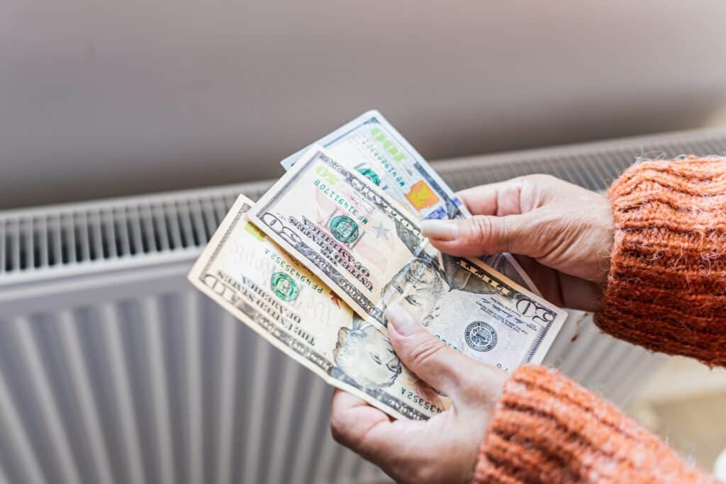 Woman holding US dollar banknotes near home radiator during winter heating season, Shutterstock ID#2804368835