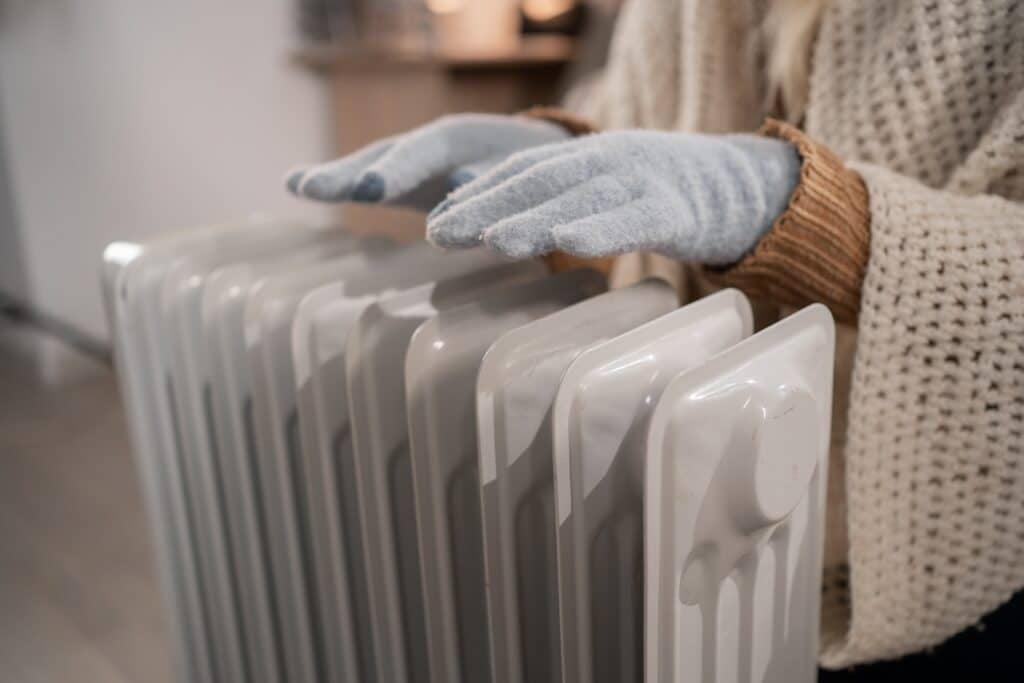 Gloved hands hover over a radiator for warmth, Shutterstock ID#2854351103